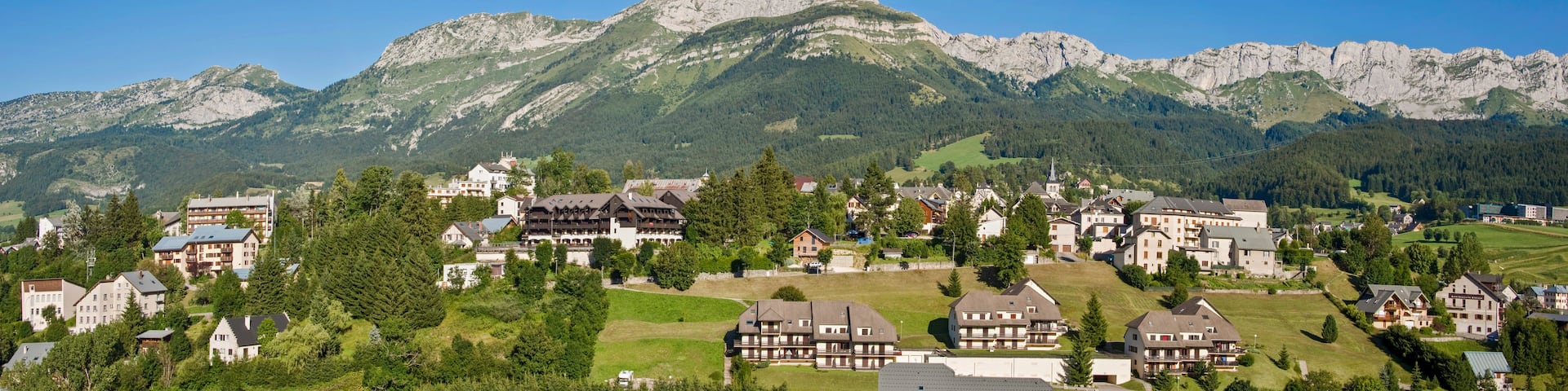 A mountain village with traditional houses, a prominent mountain peak, and lush greenery.