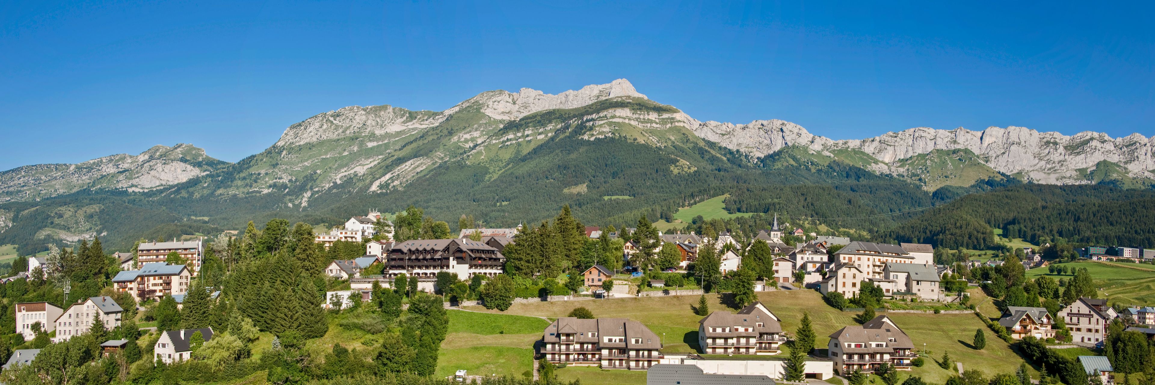 A mountain village with traditional houses, a prominent mountain peak, and lush greenery.