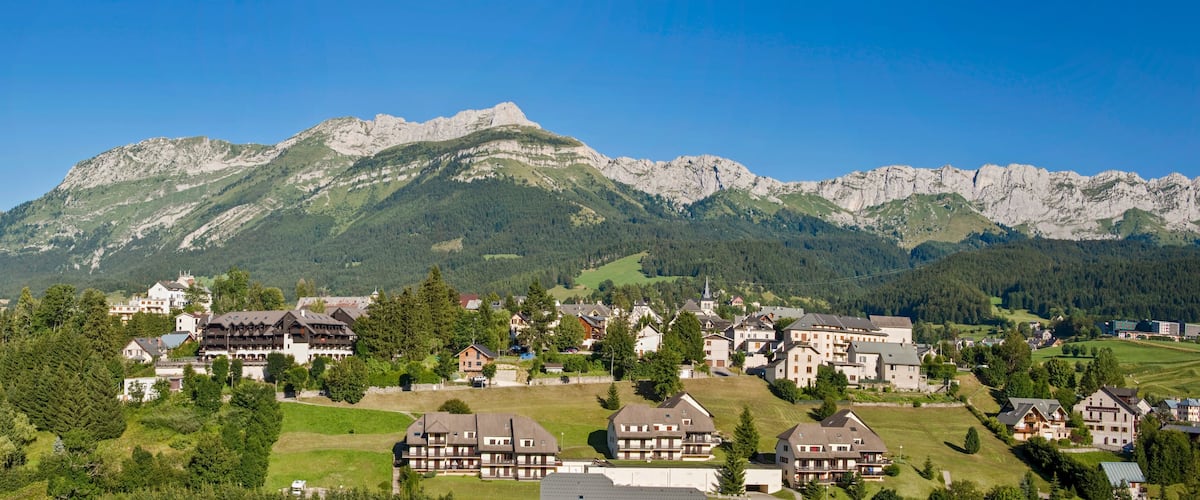 A mountain village with traditional houses, a prominent mountain peak, and lush greenery.