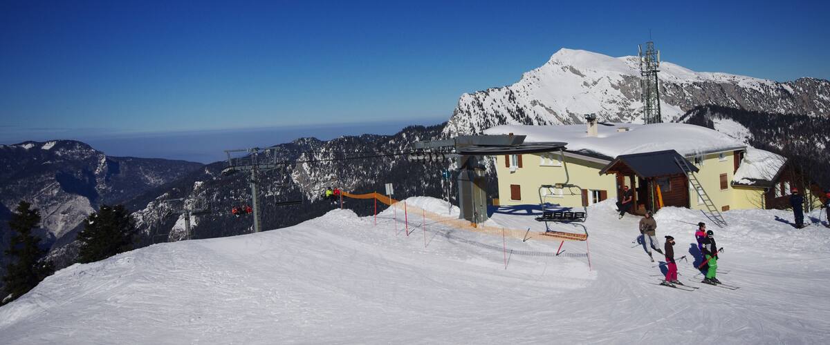 A snowy mountain landscape with a ski lift, a wooden cabin, and a clear blue sky.