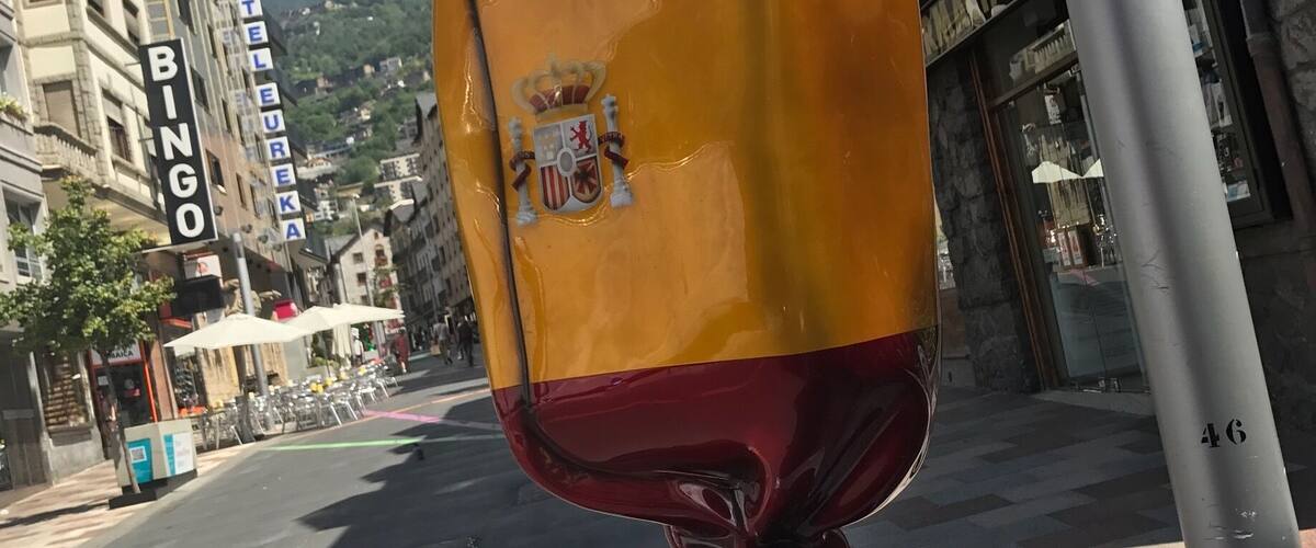 A sculpture of a red and yellow object with a coat of arms on a pedestal in an urban setting.