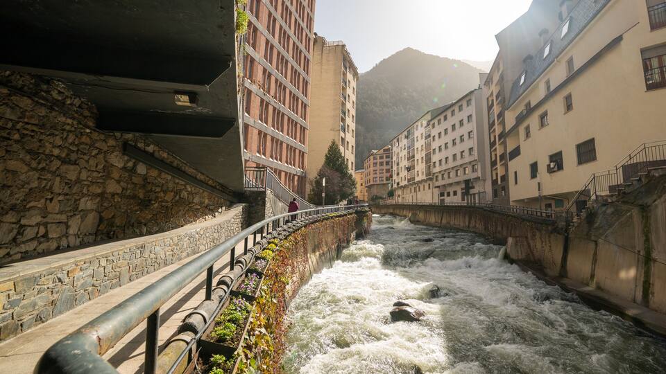 A river flowing through a stone-walled urban area with buildings on either side.