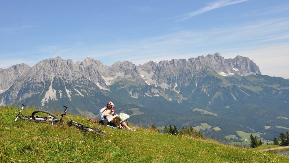 Une personne assise sur une colline herbeuse, avec une chaîne de montagnes en arrière-plan.