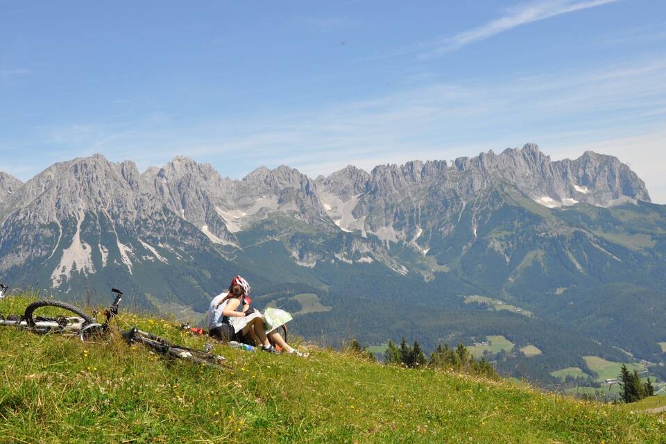 A person sitting on a grassy hill with a mountain range in the background.