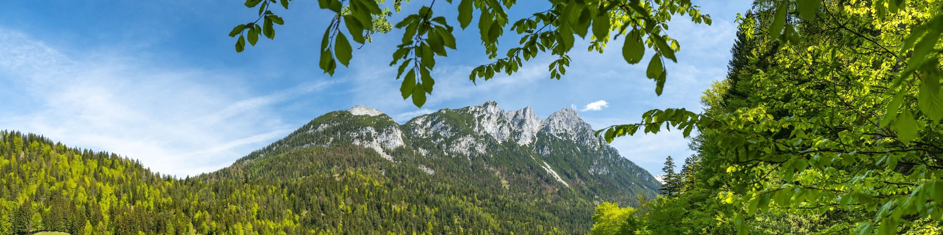 A mountain lake with clear reflections, surrounded by dense forest and a small cabin.