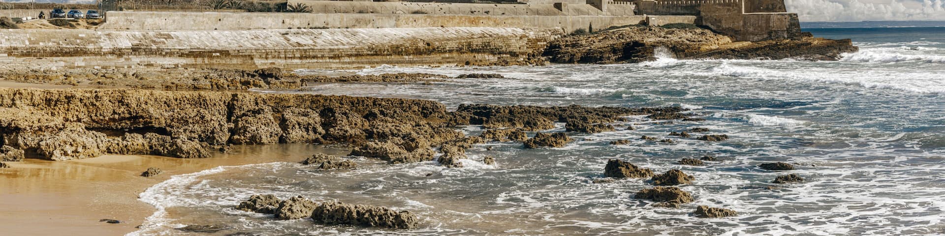 A coastal fortification with a prominent tower, waves crashing against the shore, and a clear blue sky.