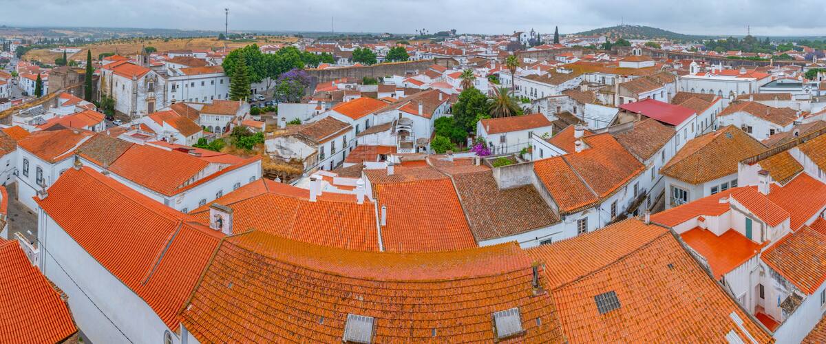 A cityscape with red-tiled rooftops, white buildings, and a distant hill.