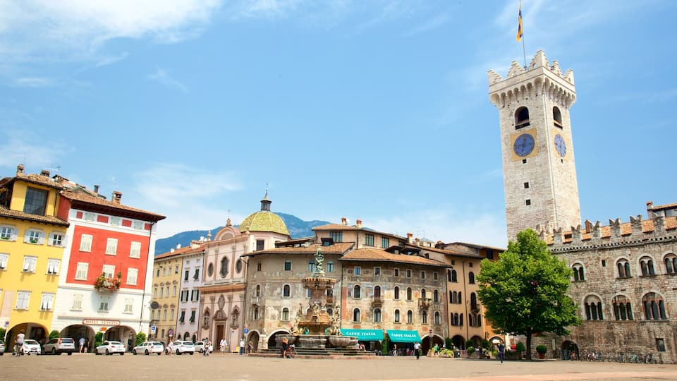 A historic square with a prominent clock tower, colorful buildings, and a fountain.