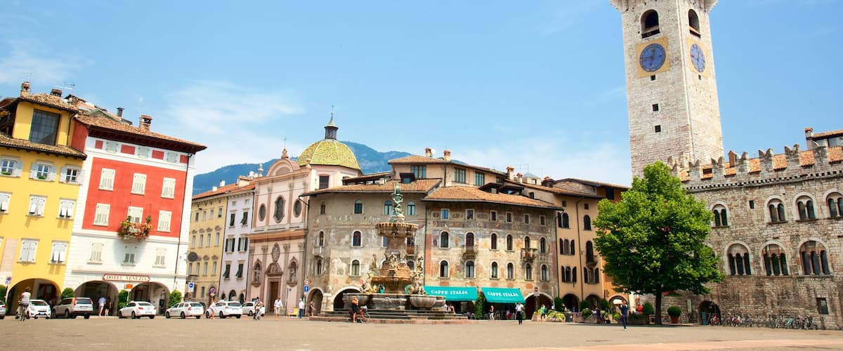 A historic square with a prominent clock tower, colorful buildings, and a fountain.