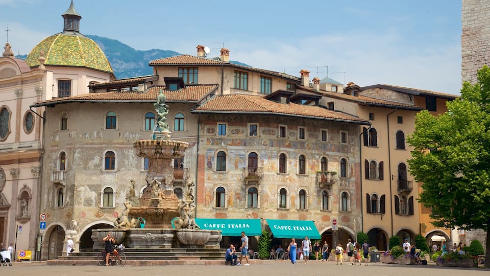 A historic building with a fountain, outdoor seating, and a mountain in the background.