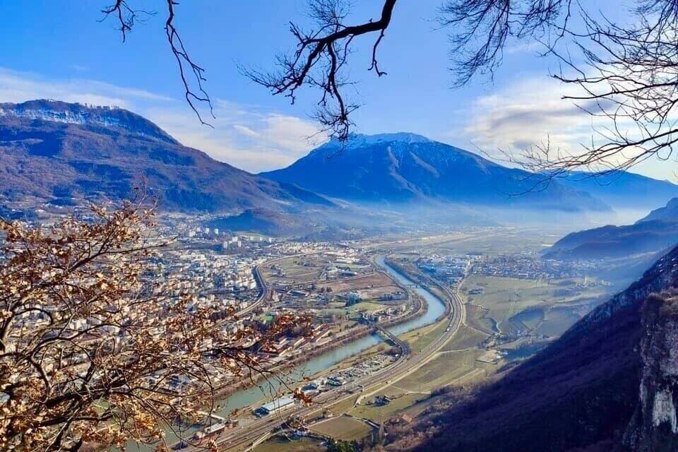 Um rio serpenteia por um vale, com montanhas ao fundo e um horizonte urbano às margens.