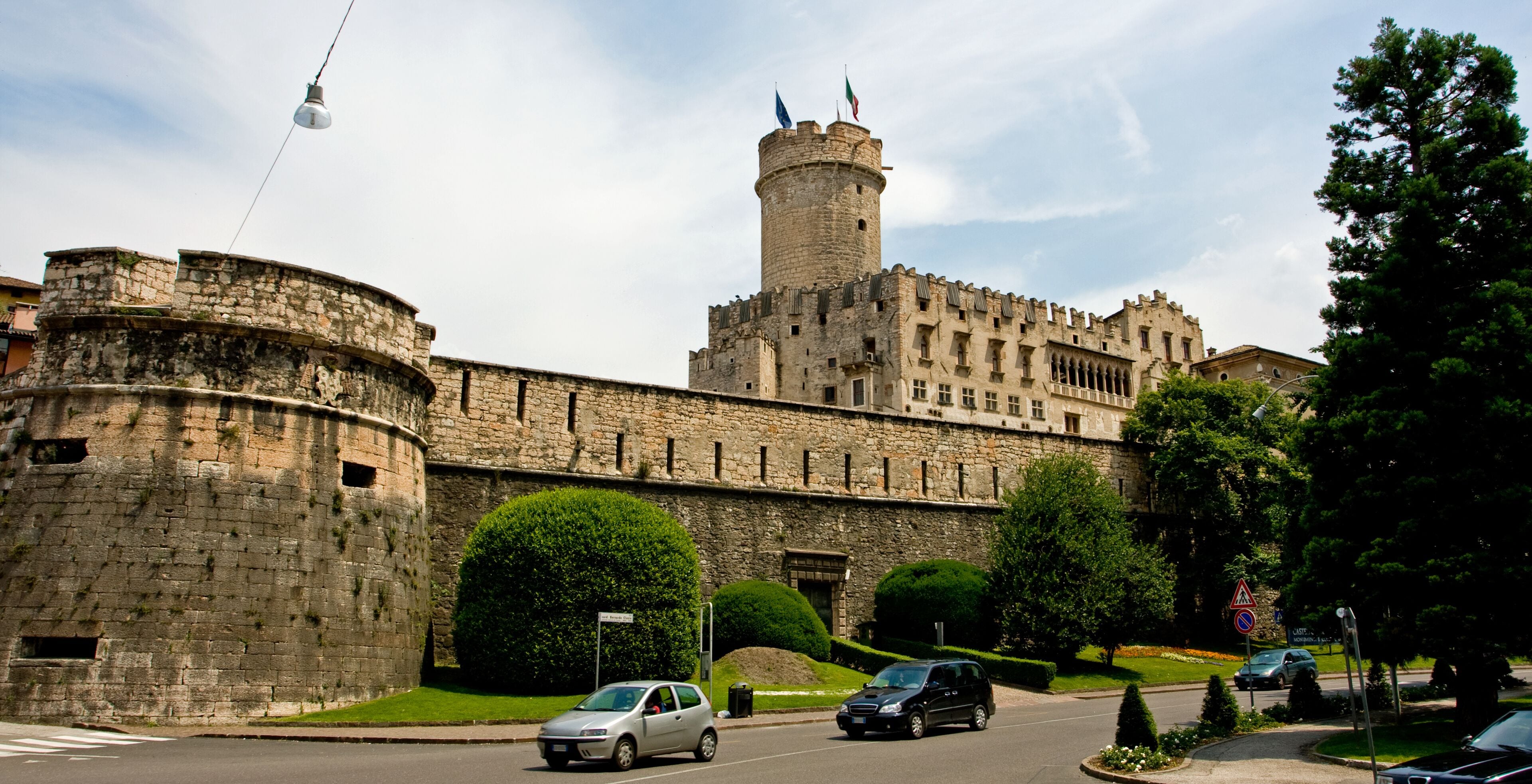 A historic castle with a tall tower, surrounded by well-maintained hedges and trees.