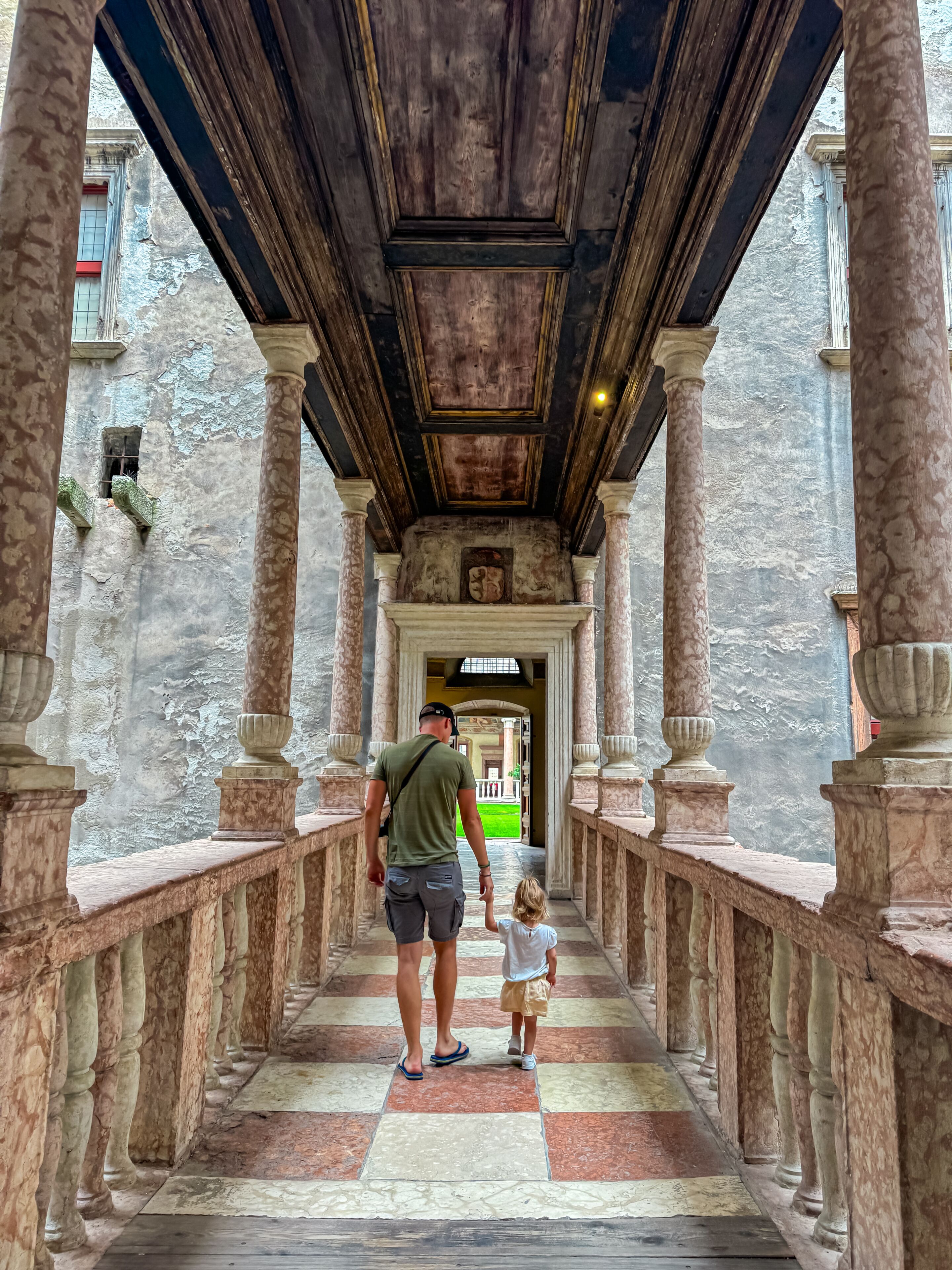 Un hombre y un niño caminando por un pasillo con columnas de mármol y techo de madera.