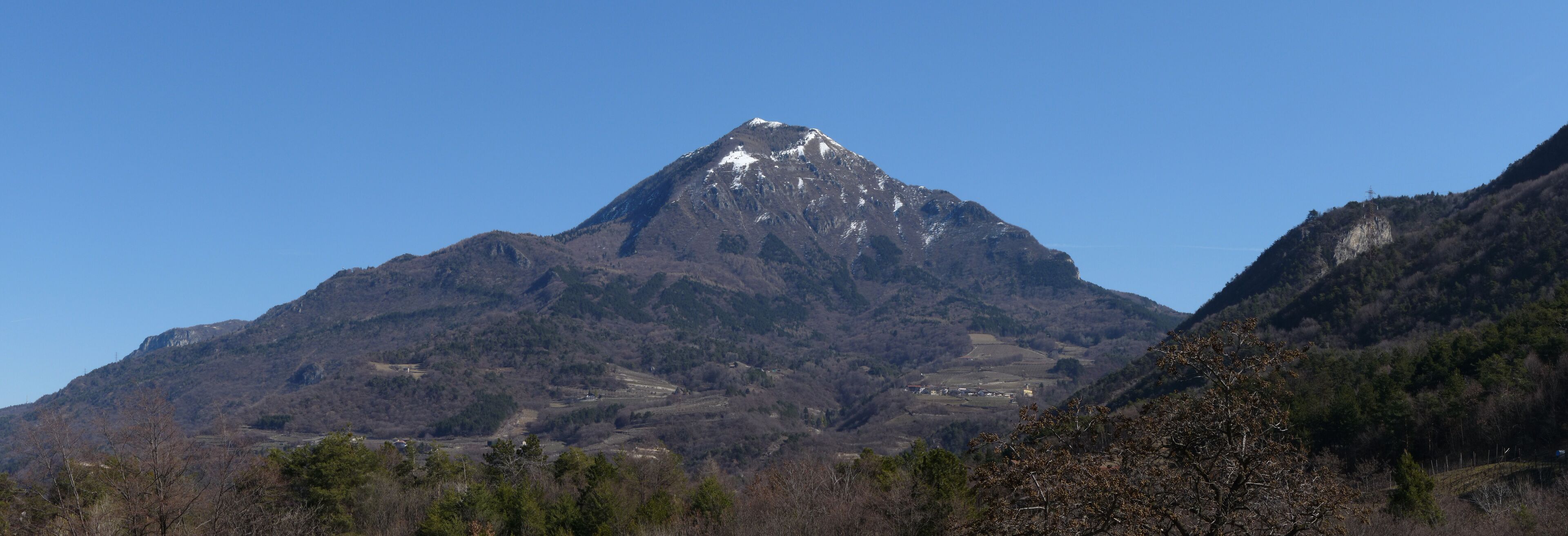 A mountain with a snow-capped peak, surrounded by forested hills.