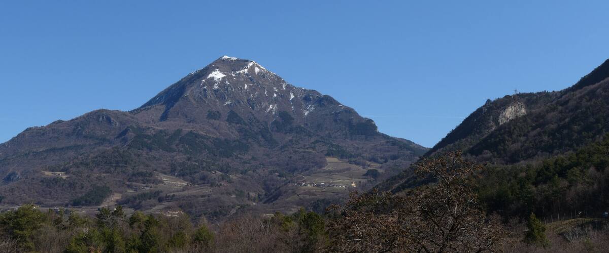 A mountain with a snow-capped peak, surrounded by forested hills.