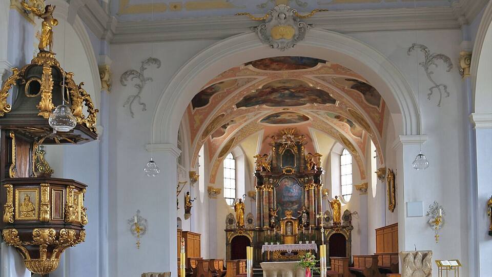 An ornate church interior with wooden pews, a central altar, and elaborate ceiling frescoes.