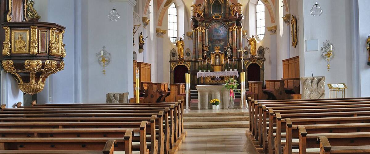 An ornate church interior with wooden pews, a central altar, and elaborate ceiling frescoes.