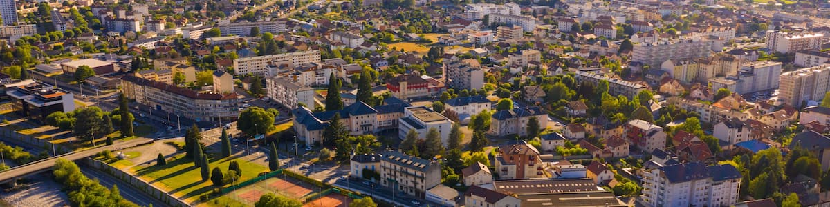 A cityscape with a river, mountains in the background, and a mix of residential and commercial buildings.