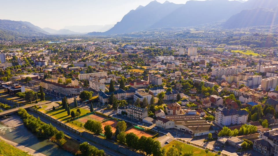 A cityscape with a river, mountains in the background, and a mix of residential and commercial buildings.