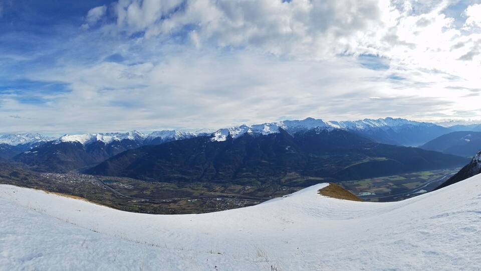 A snow-covered mountain landscape with a valley and distant peaks.