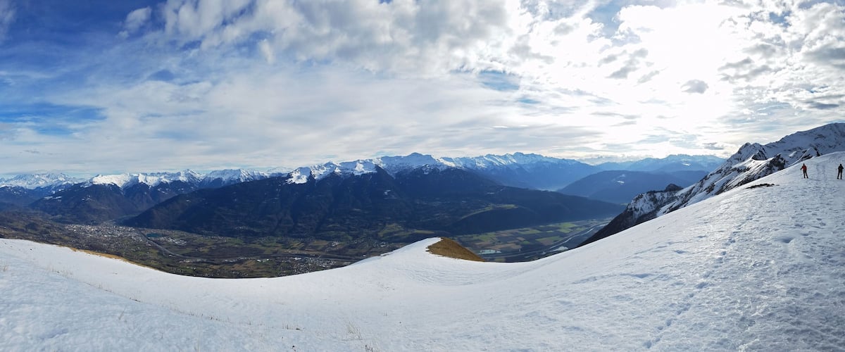 A snow-covered mountain landscape with a valley and distant peaks.
