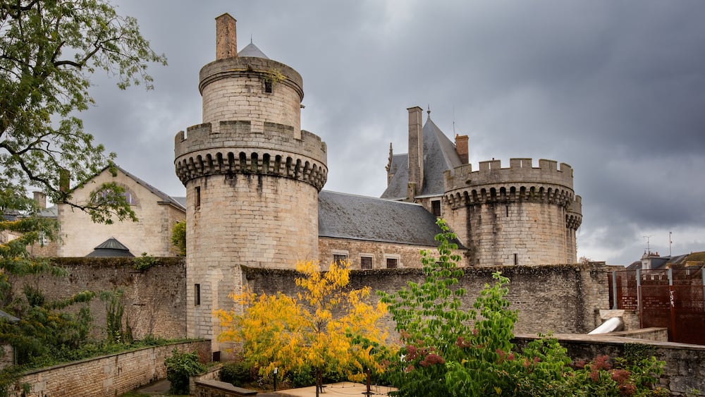 Un château historique doté de deux tours imposantes, entouré d’un jardin bien entretenu et d’un mur de pierre.