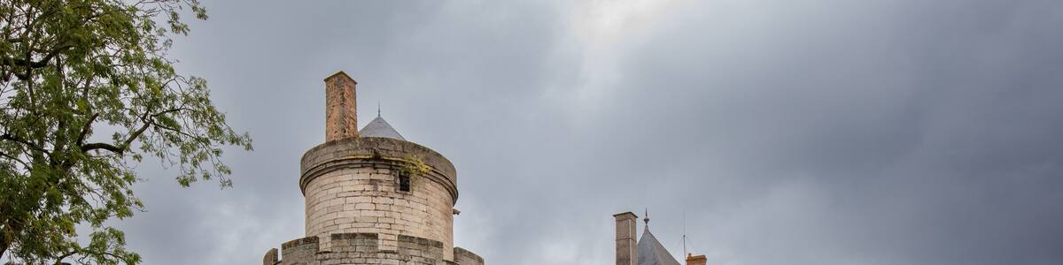 Un château historique doté de deux tours imposantes, entouré d’un jardin bien entretenu et d’un mur de pierre.