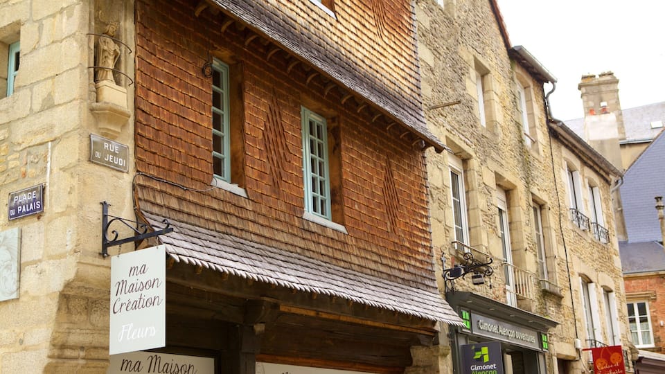 A historic building with wooden shutters, stone walls, and signs indicating 'Place du Palais' and 'Maison Création'.