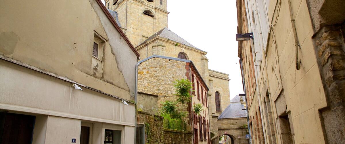 A narrow street with historic stone buildings, a church with a bell tower, and a pedestrian.