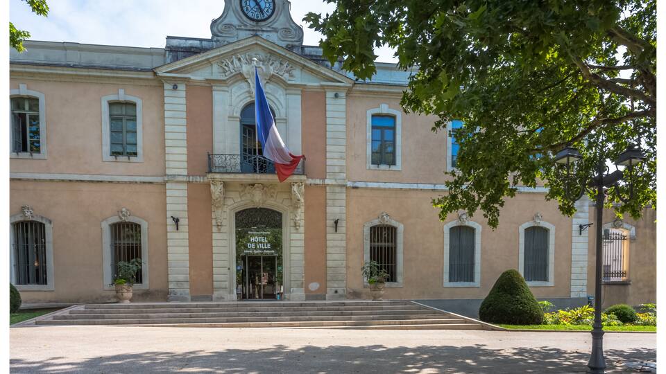 A historic building with a clock tower, a flag, and a well-maintained entrance.