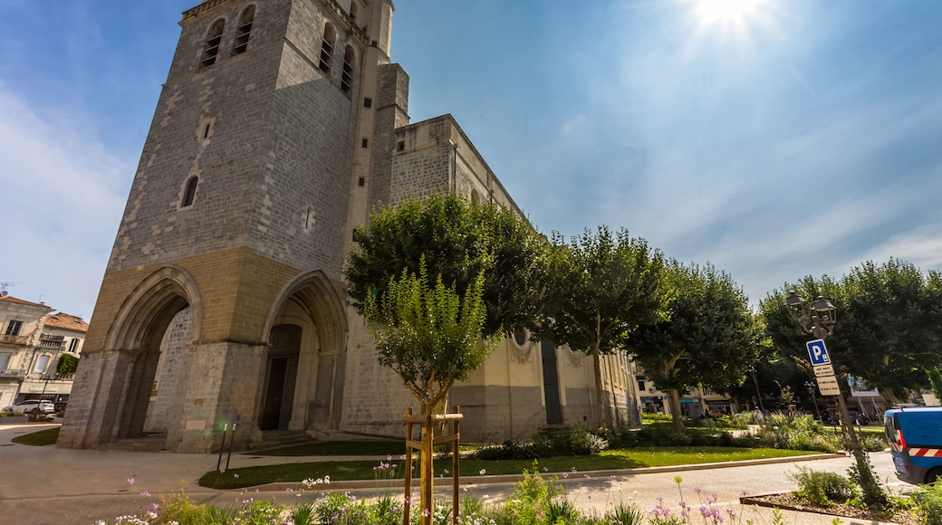 A historic stone church with a bell tower, surrounded by a well-maintained garden and a clear blue sky.