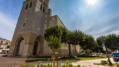 A historic stone church with a bell tower, surrounded by a well-maintained garden and a clear blue sky.