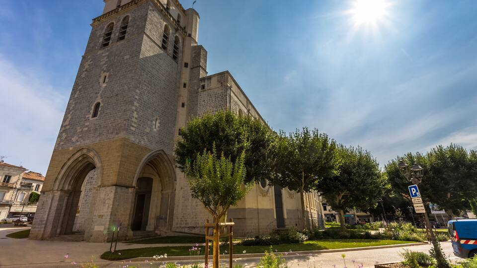A historic stone church with a bell tower, surrounded by a well-maintained garden and a clear blue sky.