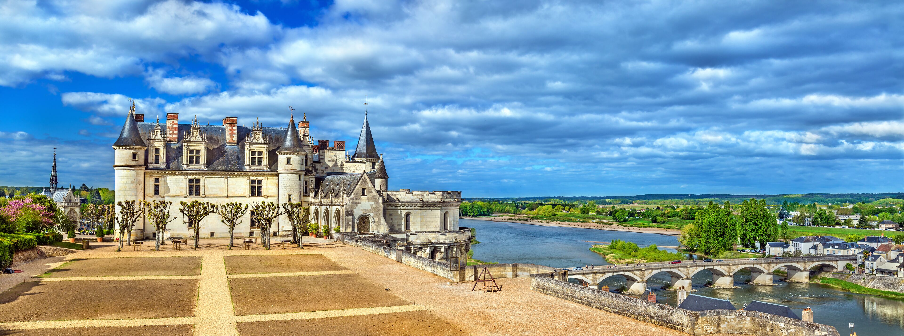 A historic castle with a river and a bridge in the background.