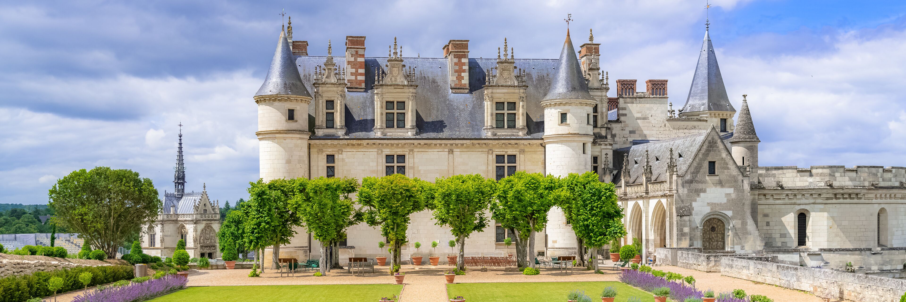 A historic castle with turrets, a courtyard, and a river in the background.