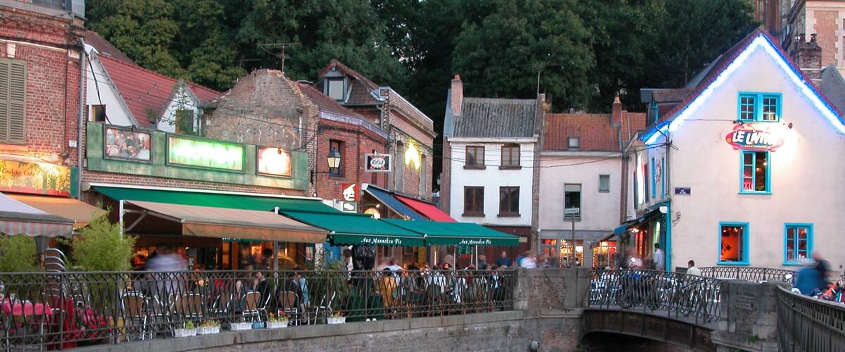 A historic town with a stone bridge over a canal, cafes, and traditional European architecture.