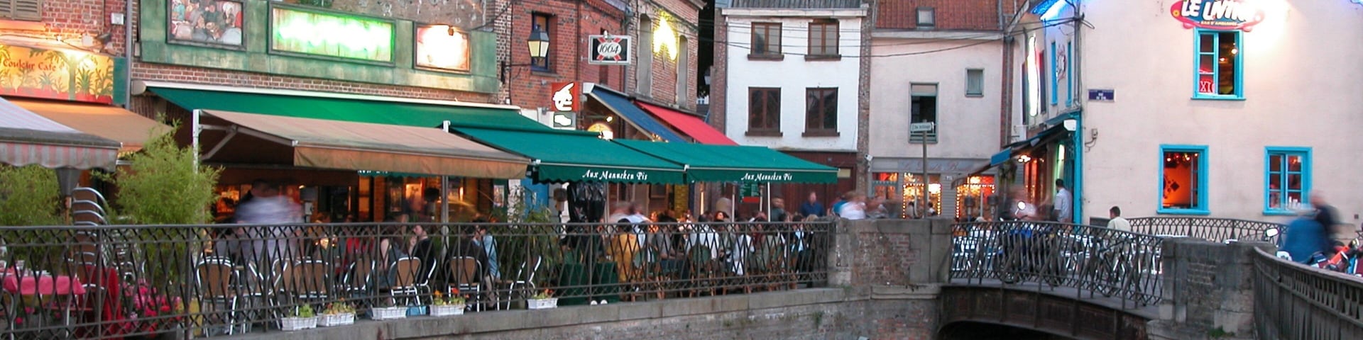 A historic town with a stone bridge over a canal, cafes, and traditional European architecture.