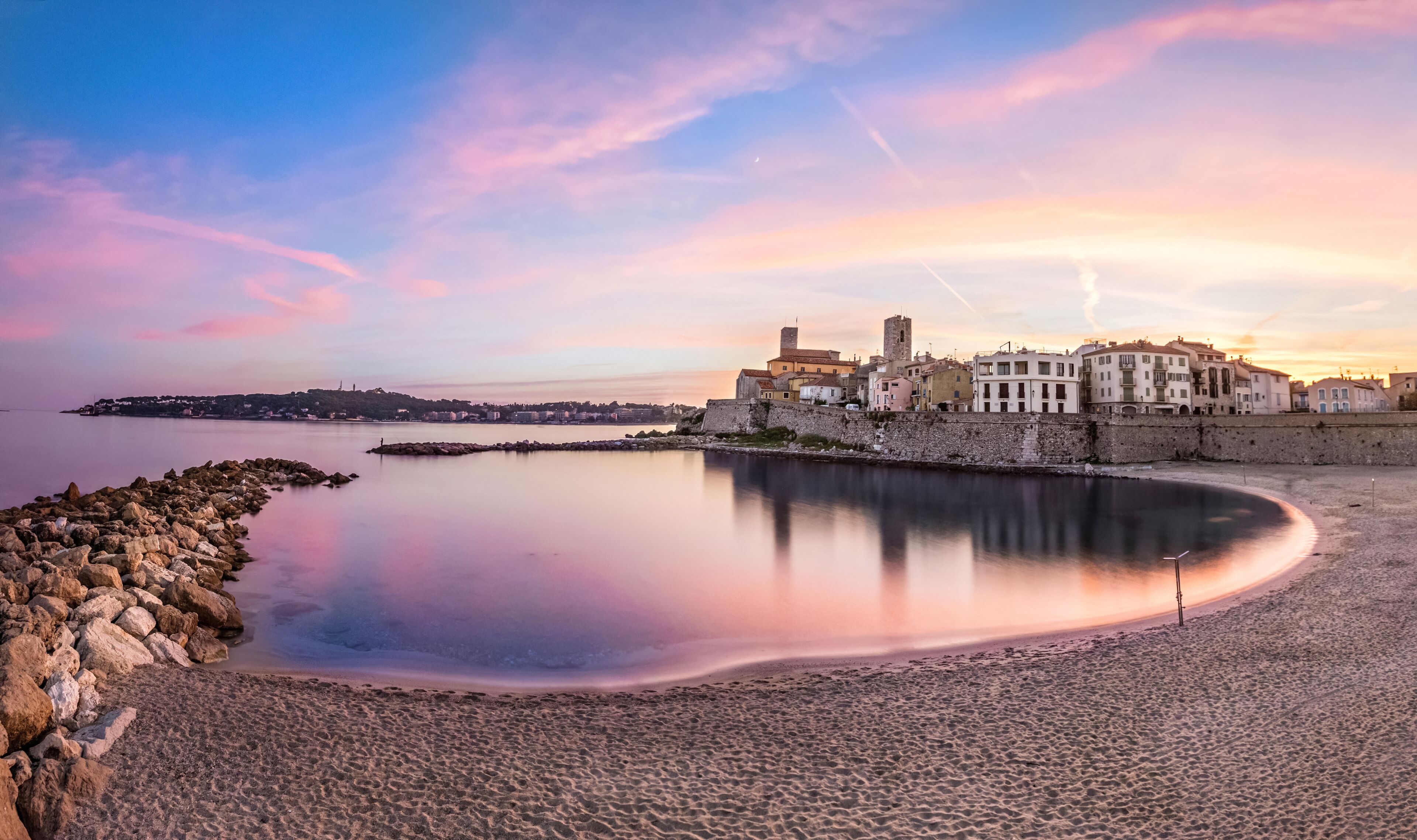 A coastal town with a calm bay, historic buildings, and a stone wall.