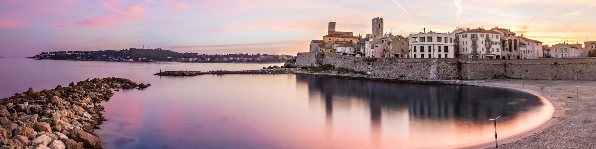 A coastal town with a calm bay, historic buildings, and a stone wall.