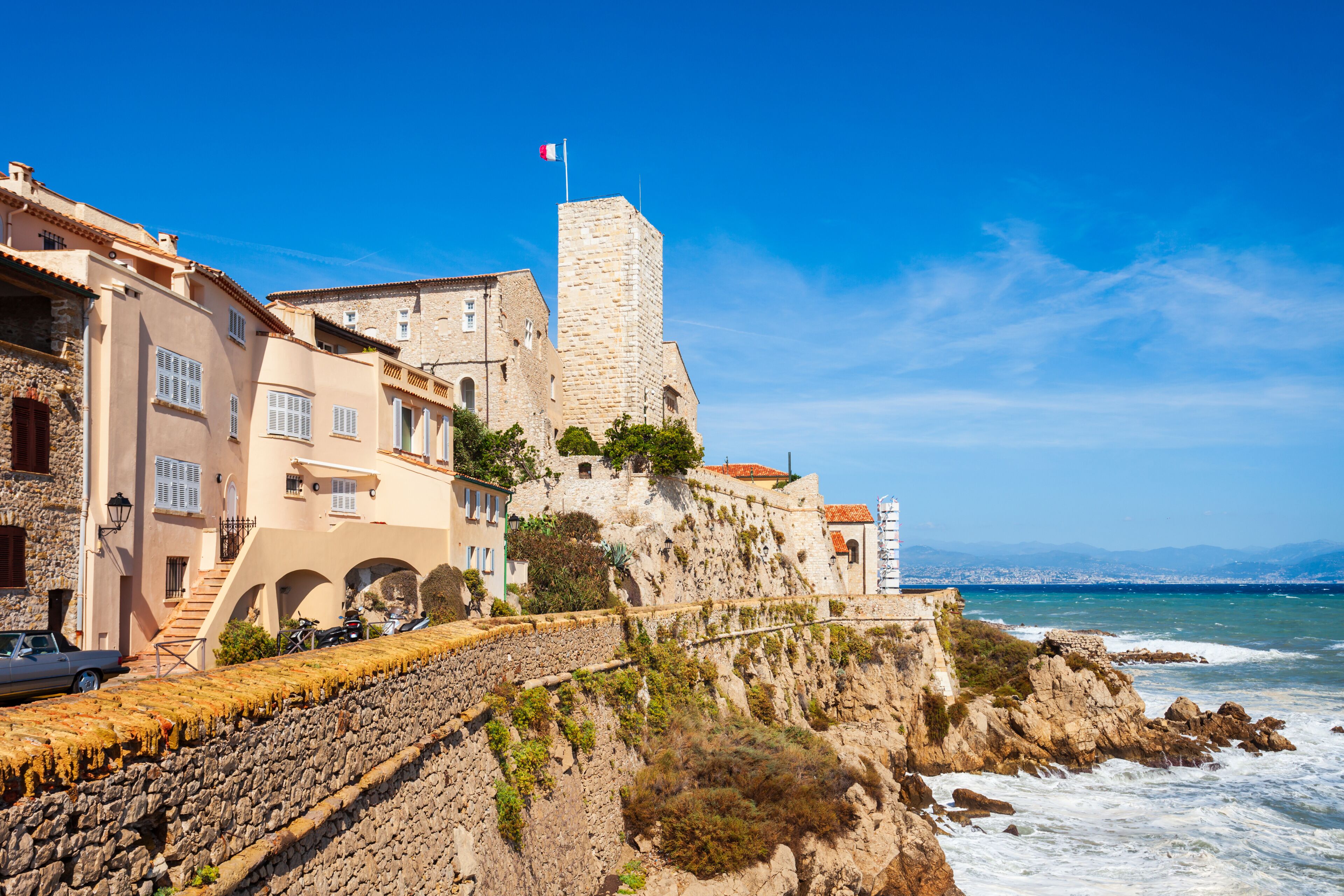 A coastal town with historic stone buildings, a prominent tower, and a stone wall overlooking the sea.