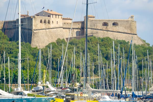 Un château historique perché sur une colline, avec un port de plaisance en contrebas où sont amarrés de nombreux voiliers.