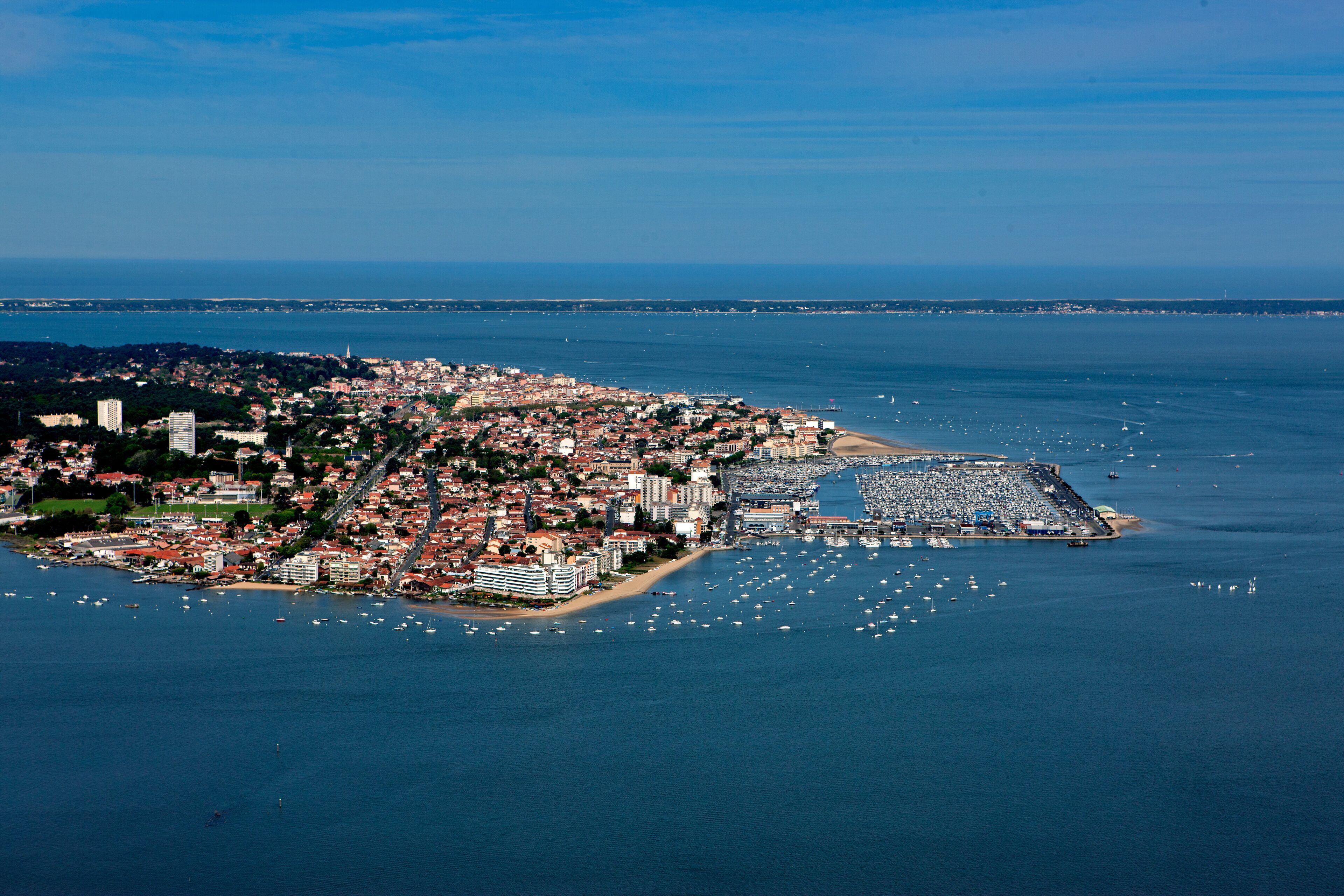 An aerial view of a coastal city with a marina, dense urban area, and a large body of water.