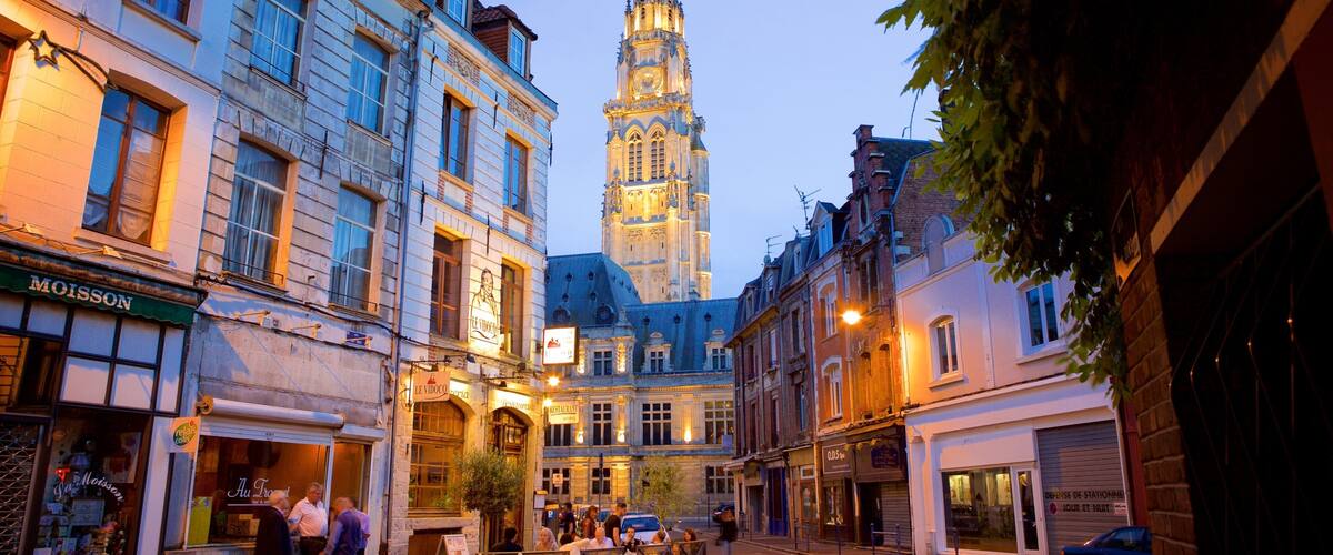 A historic European town square with a prominent tower, shops, and pedestrians.