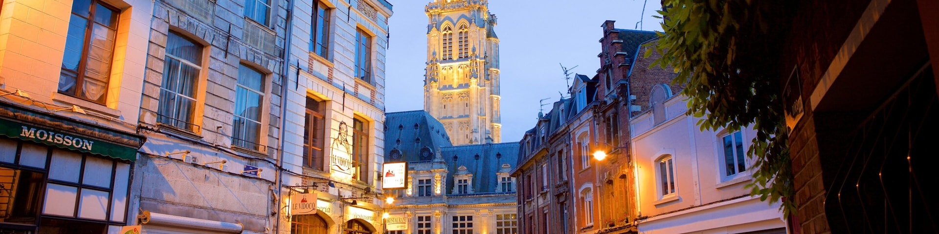 A historic European town square with a prominent tower, shops, and pedestrians.