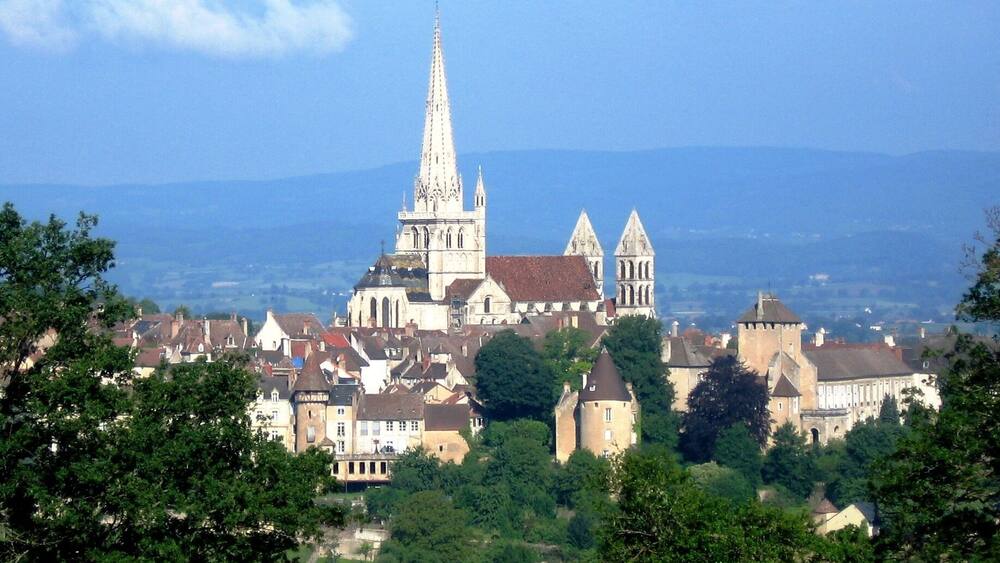 Une cathédrale dotée d’une haute flèche, entourée de bâtiments historiques et d’arbres.