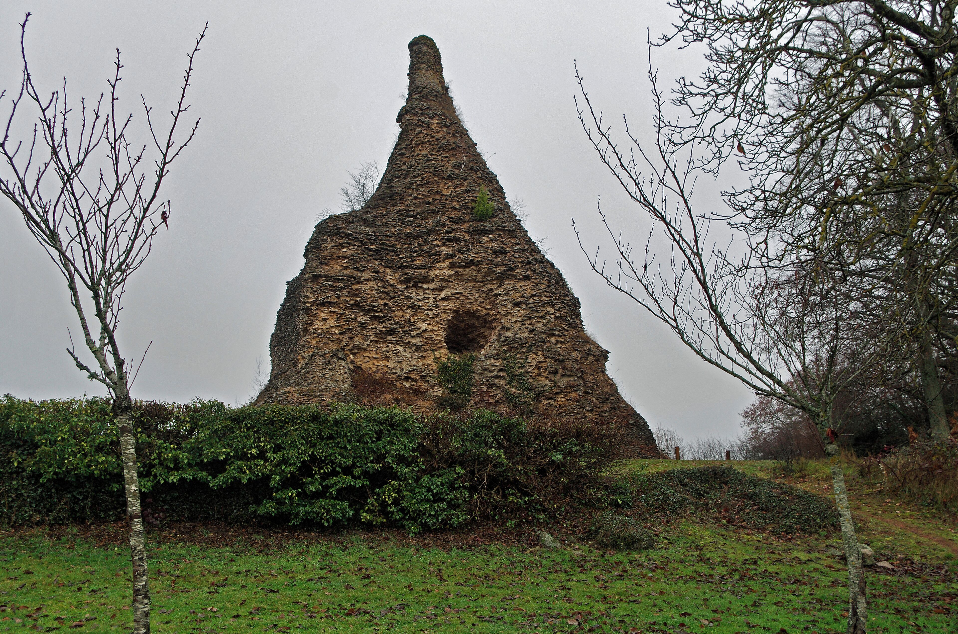 Autun (Saône-et-Loire) La Pyramide de Couhard (ou Pierre de Couhard). Le nom est celui du hameau de Couhard situé dans les hauteurs d'Autun. La ville d'Autun (Augustodunum)a été fondée par les Romains vers la fin du 1er siècle. Elle est la ville nouvelle remplaçant Bibracte, capitale des Eduens située sur le Mont-Beuvray. La France compte quatre pyramides connues : à Falicon, près de Nice, à Couhard, près d’Autun, à Plouézoch et à Carnac. Mais il y en eut certainement d'autres. La pyramide de Couhard daterait du Ier siècle. Sa hauteur d'origine devait atteindre 33 mètres. La forme devait être pyramidale. La tradition veut que la pyramide fut autrefois recouverte de marbre, mais ce fut plus probablement de calcaire blanc. Le parement aurait été arraché et réutilisé dans la construction de l'église et des maisons de Couhard, il ne reste que le blocage*. La pente qui descend depuis la pyramide vers la ville était en partie occupée par une nécropole, le Champ des Urnes. Cette nécropole s'étendait le long de la voie d'Agrippa (en direction de Chalon). Un médaillon d'or retrouvé sur place avec ces mots "Gloria Aedorum druidumque" laisse penser que cette pyramide servit de tombeau à Dividiacus, célèbre druide de la région. En 1640, l'abbé de Castille fit creuser l'édifice afin de découvrir une chambre intérieure. Recherche infructueuse, l'édifice étant plein. En 1960, lors de travaux de consolidation, on découvrit une plaquette de plomb, probablement du IIe siècle, avec des inscriptions certainement en rapport avec un rite magique, tablette conservée au musée Rolin. Cette tablette de 16cm sur 6, porte des inscriptions maléfiques en latin et en grec, ainsi qu’une grande croix. Blocage : type de maçonnerie appelée "opus caementicium", qui utilise du mortier, formé d'un mélange de sable (ou de pouzzolane) et de chaux, pour lier de petits blocs de roche concassée.