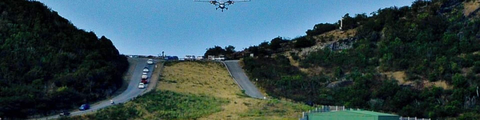 A coastal road leading to a beach with a clear sky and an airplane in the distance.