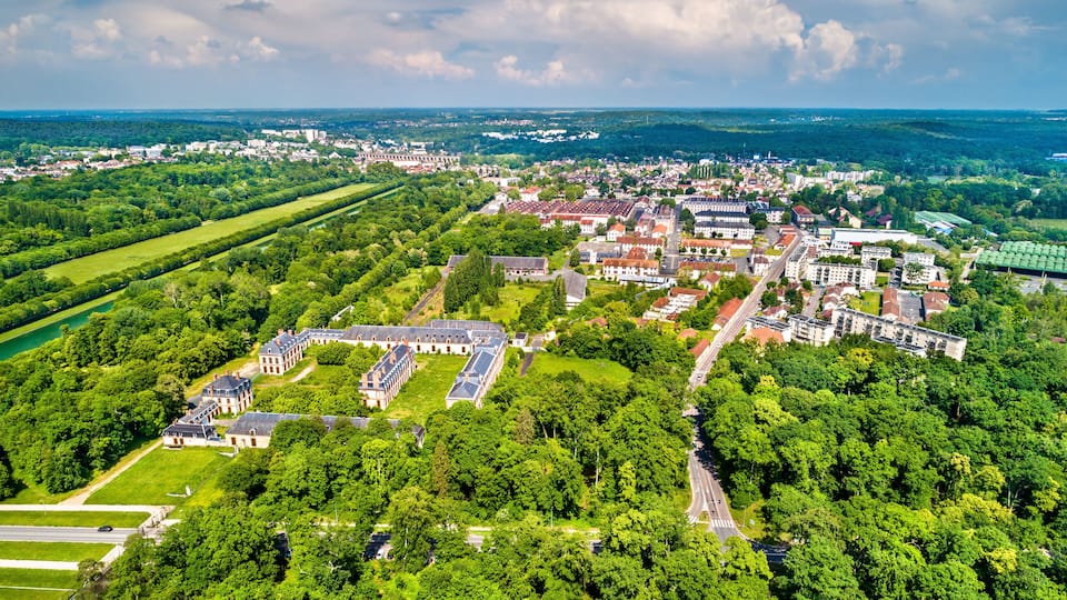 An aerial view of a town with a large historic building complex surrounded by lush greenery and a river.