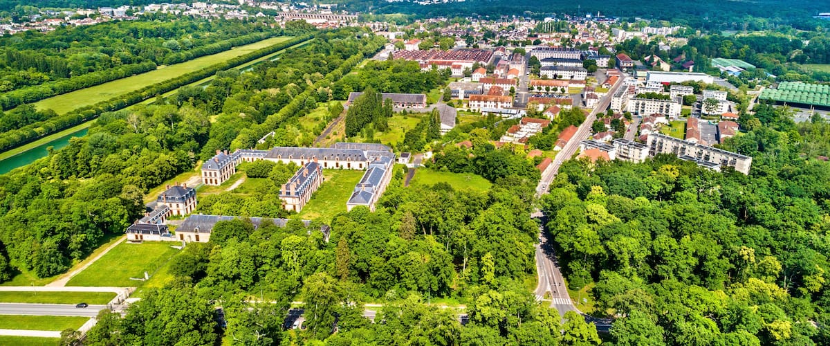 An aerial view of a town with a large historic building complex surrounded by lush greenery and a river.