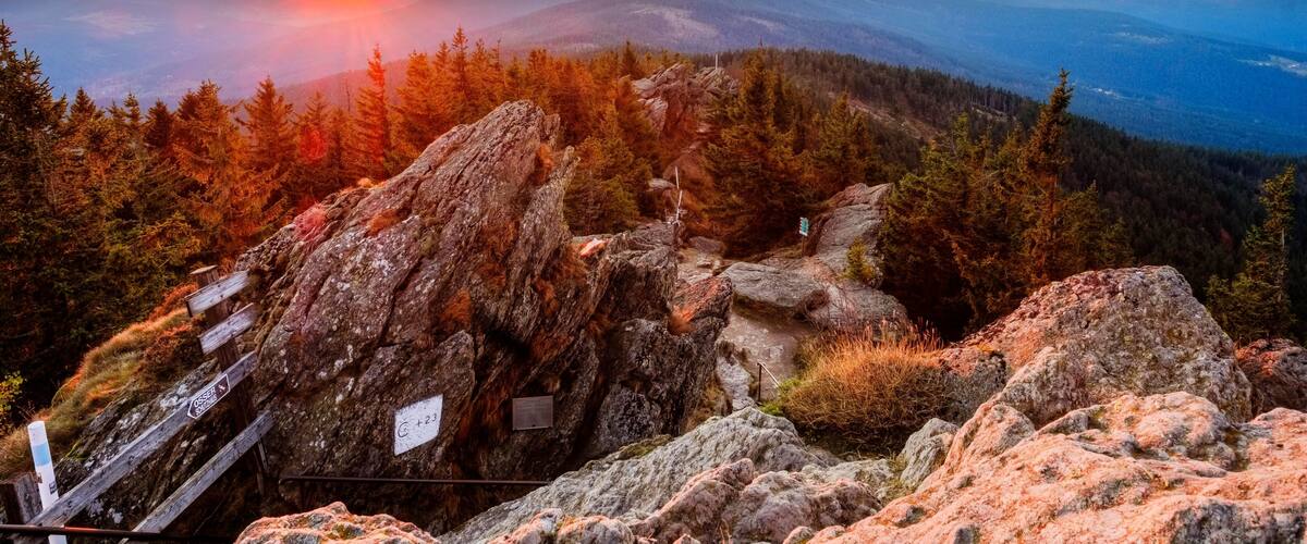 A mountainous landscape with a sunset, rocky terrain, and a trail marked by signs.